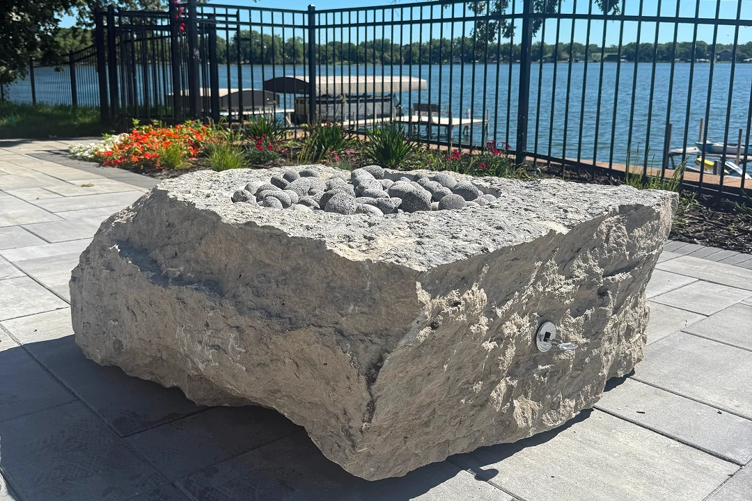 Large stone sculpture by a lakeside fence.